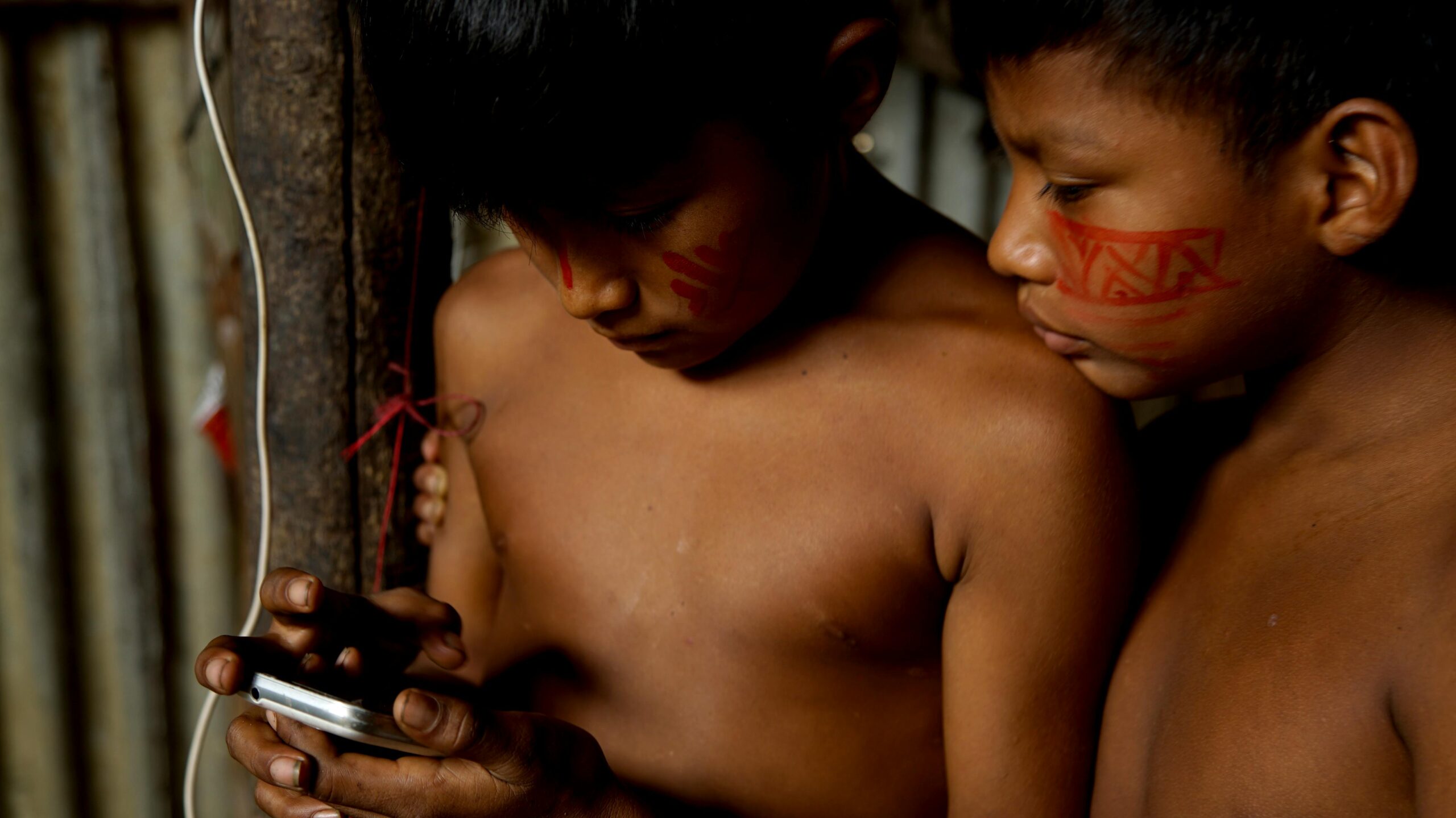 Zwei indigene Kinder aus dem Amazonasgebiet erkunden drinnen ein Smartphone.