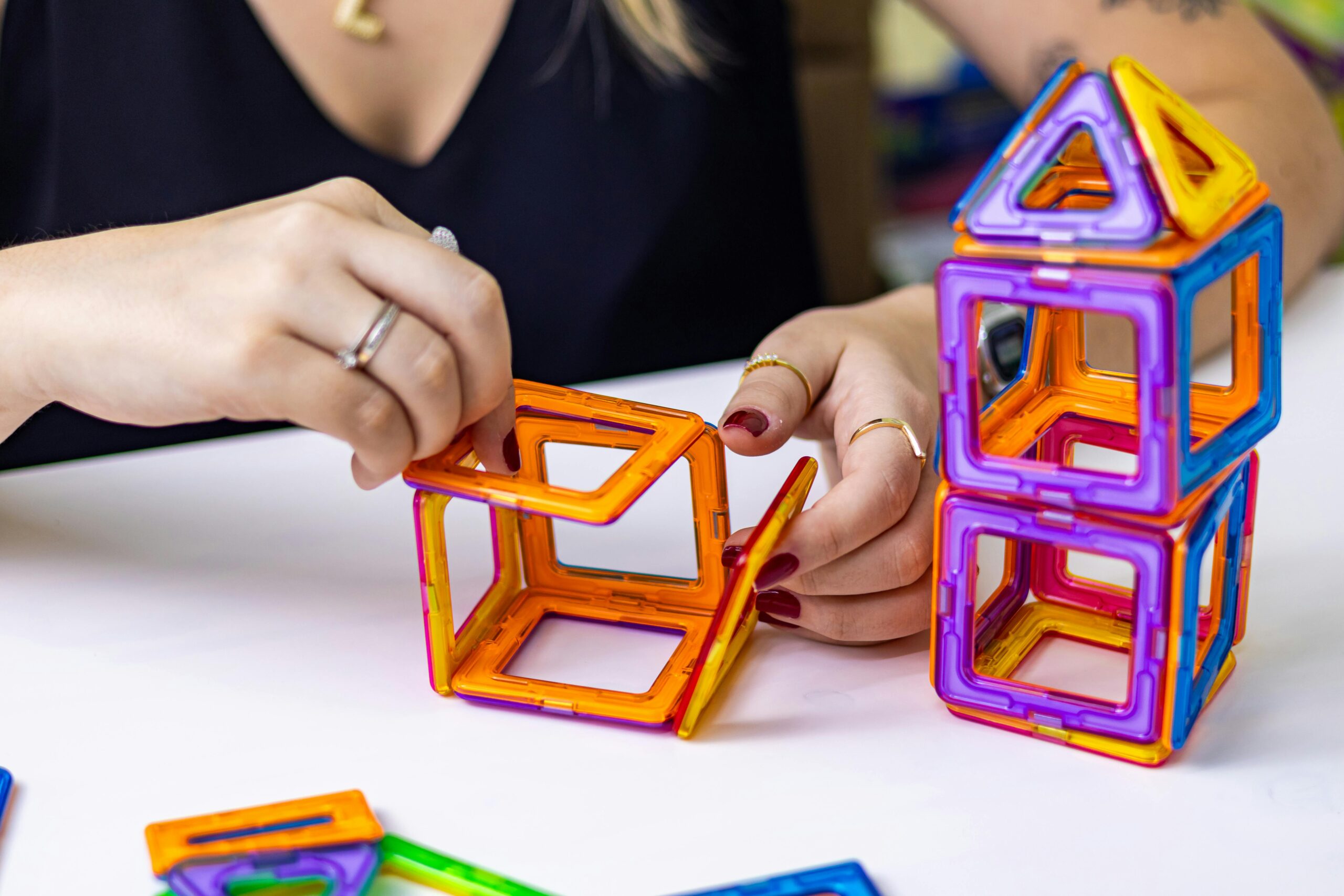 FrauenhÃ¤nde bauen bunte magnetische SpielzeugblÃ¶cke im Innenbereich fÃ¼r Bildung und KreativitÃ¤t.