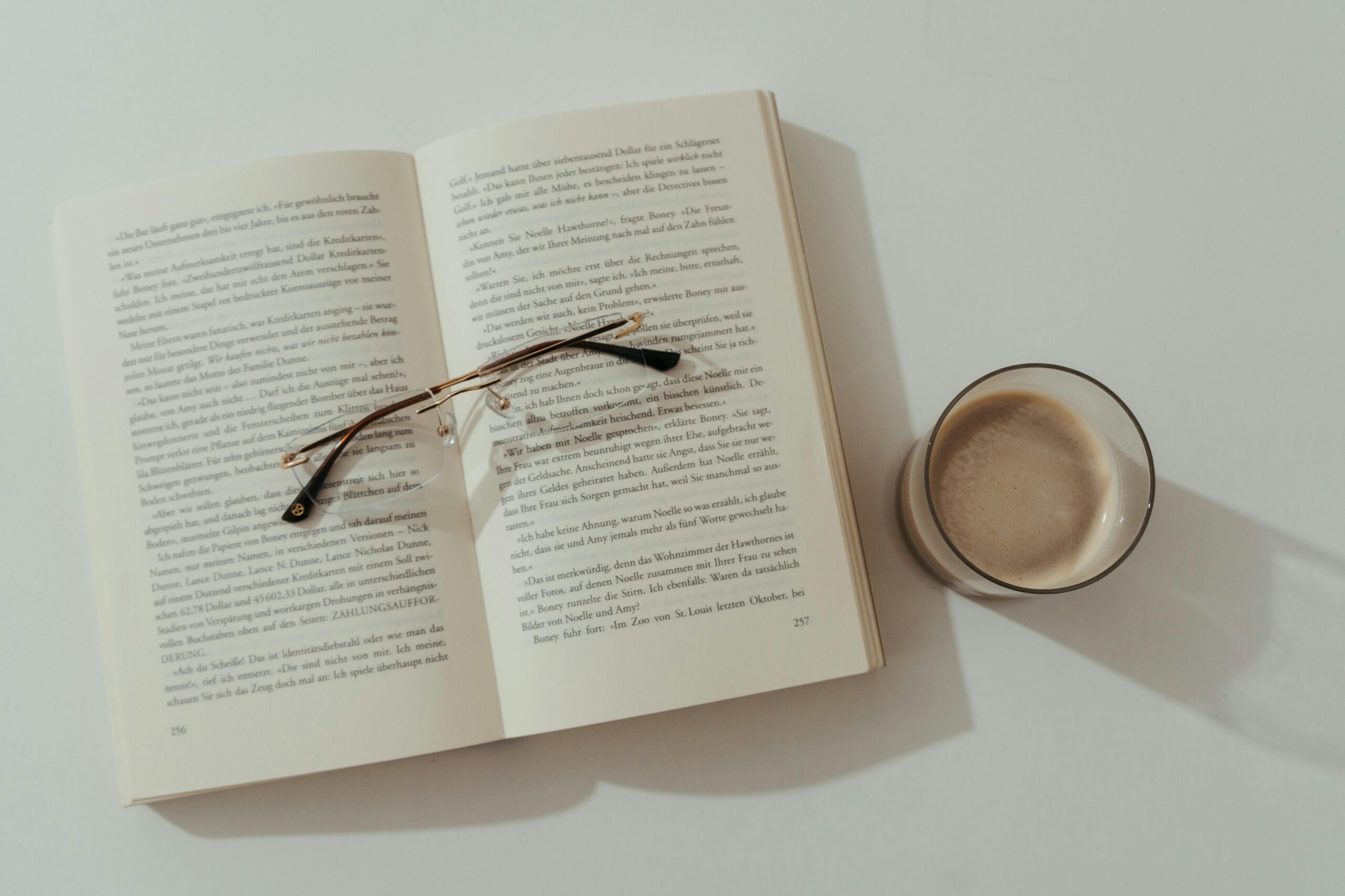 Eine gemÃ¼tliche Szene mit einem offenen Buch, einer Brille und Kaffee auf einem weiÃŸen Tisch, perfekt fÃ¼r Buchliebhaber.