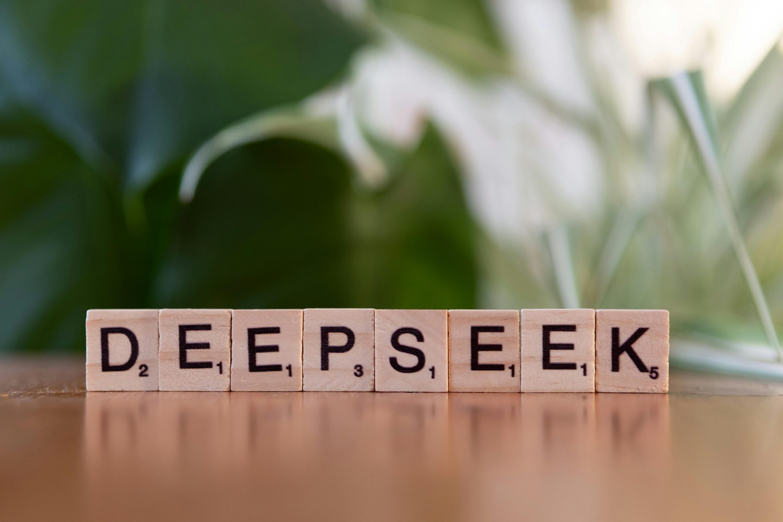 HÃ¶lzerne Buchstabensteine mit der Aufschrift â€žDEEPSEEKâ€œ auf einem Tisch mit verschwommenem grÃ¼nem Hintergrund.