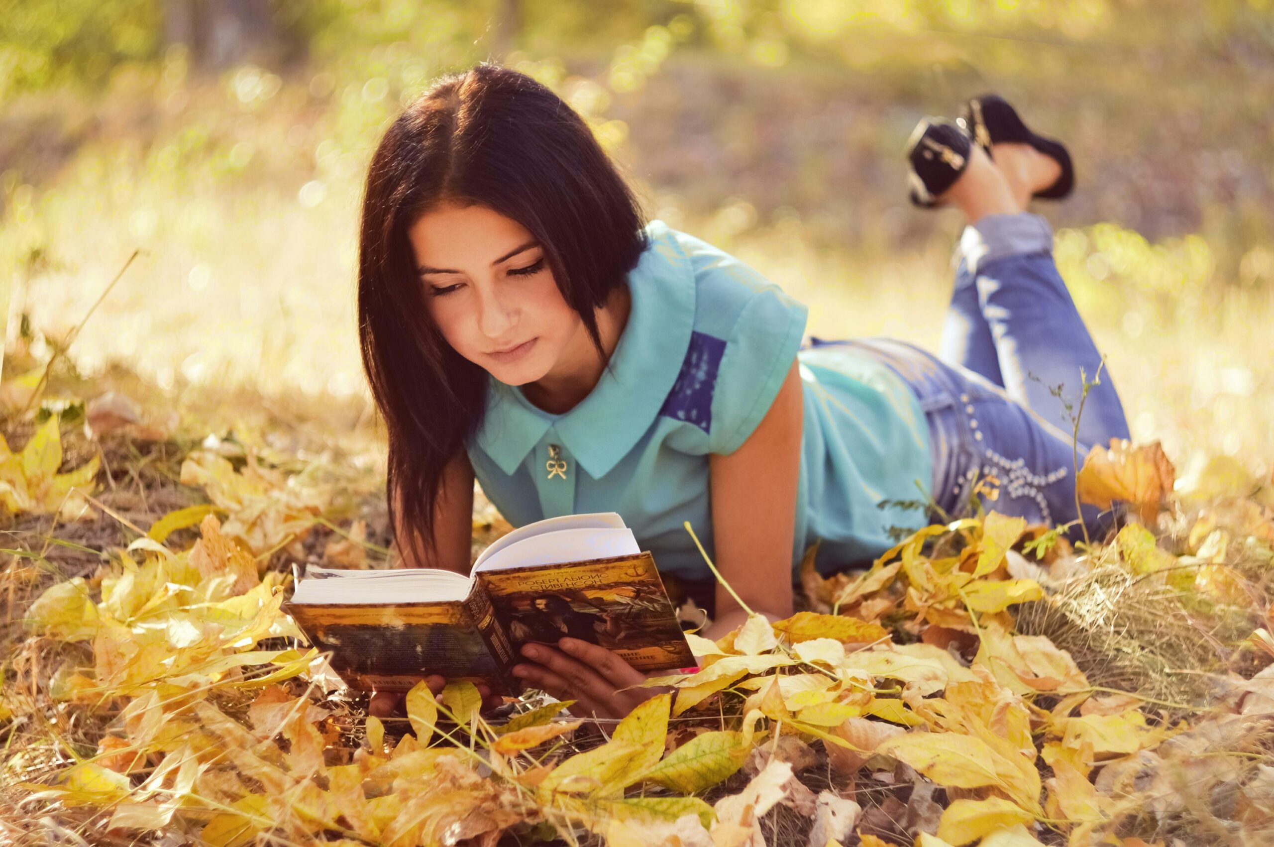 Eine junge Frau liest gerne ein Buch, wÃ¤hrend sie in einem sonnigen Park im Herbstlaub liegt.